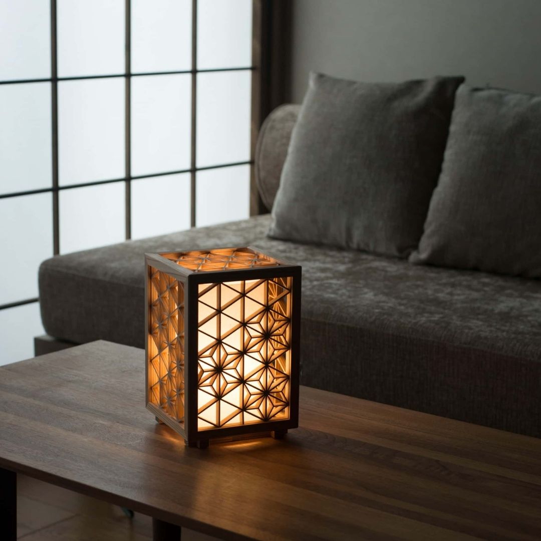 Japanse Kumiko lamp "Asanoha" klein die een warme gloed uitstraalt op de houten tafel in een schemerige woonkamer in Japanse stijl