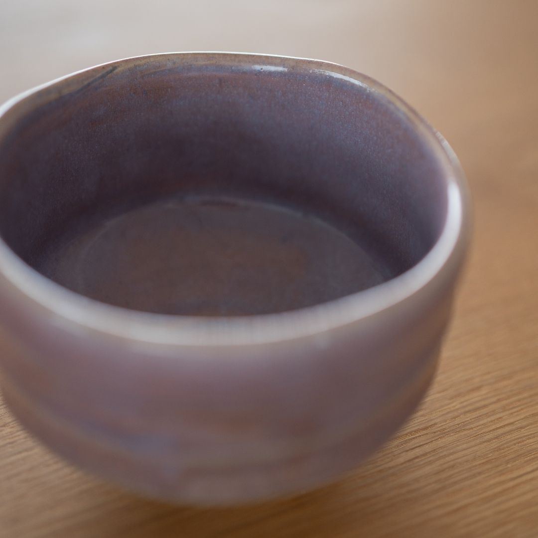 Nahaufnahme einer blassvioletten japanischen Matcha-Schale von Shinzan Kiln, die die glänzende hellviolette Glasur und die warmen Erdtöne des Mino-Ware auf der texturierten Oberfläche zeigt.