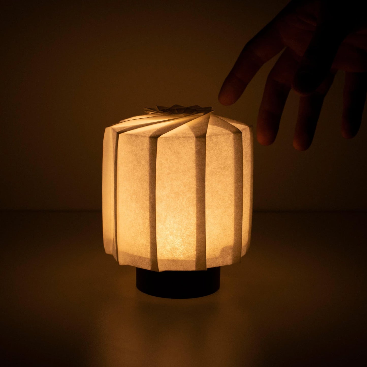 "Hand die een frameloze Japanse tafellamp vasthoudt, vervaardigd met traditionele Kyo-hyogu en origami-technieken, met een uniek verlicht origami-patroon. met de hand"