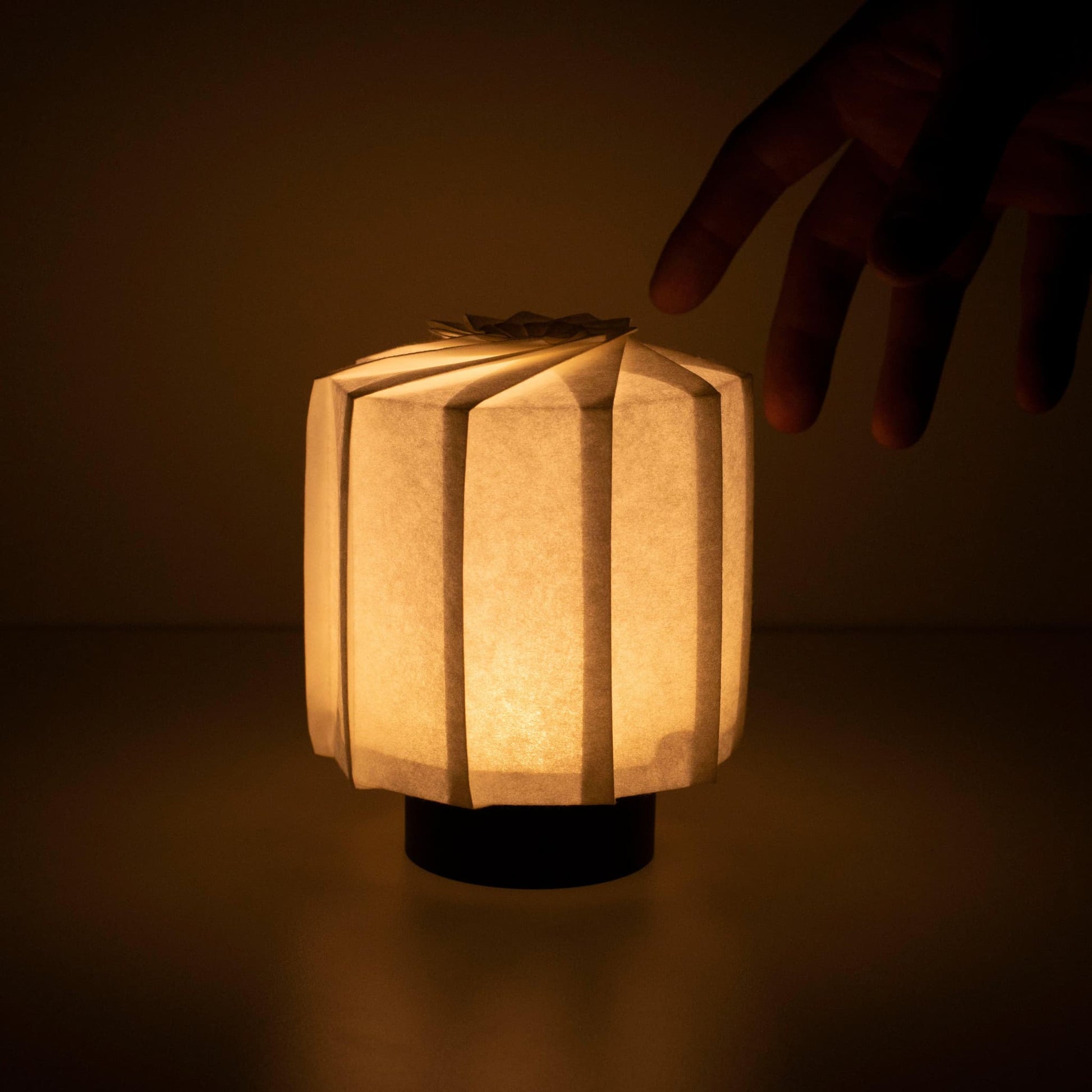 "Hand die een frameloze Japanse tafellamp vasthoudt, vervaardigd met traditionele Kyo-hyogu en origami-technieken, met een uniek verlicht origami-patroon. met de hand"