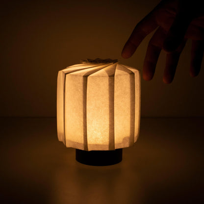 "Hand die een frameloze Japanse tafellamp vasthoudt, vervaardigd met traditionele Kyo-hyogu en origami-technieken, met een uniek verlicht origami-patroon. met de hand"
