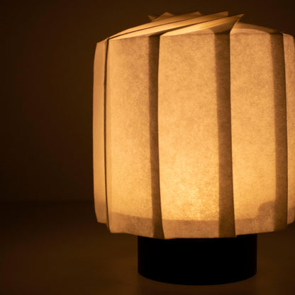 Hand die een frameloze Japanse papieren tafellamp vasthoudt, vervaardigd met traditionele Kyo-hyogu en origami-technieken, met een uniek verlicht origami-patroon.