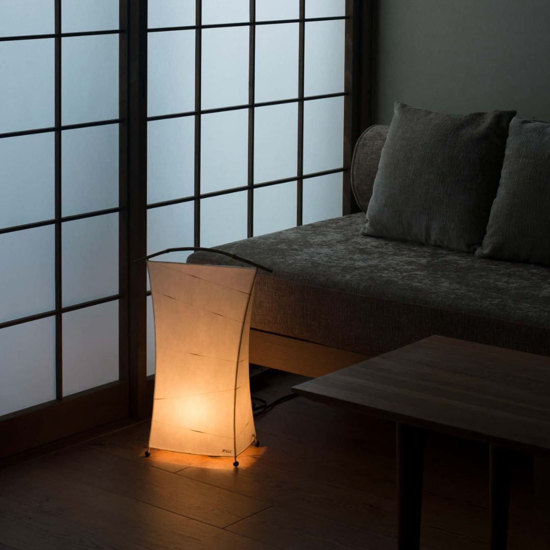 "Lampe japonaise au sol diffusant un halo chaleureux « NOW » dans le coin d'un salon japonais faiblement éclairé"