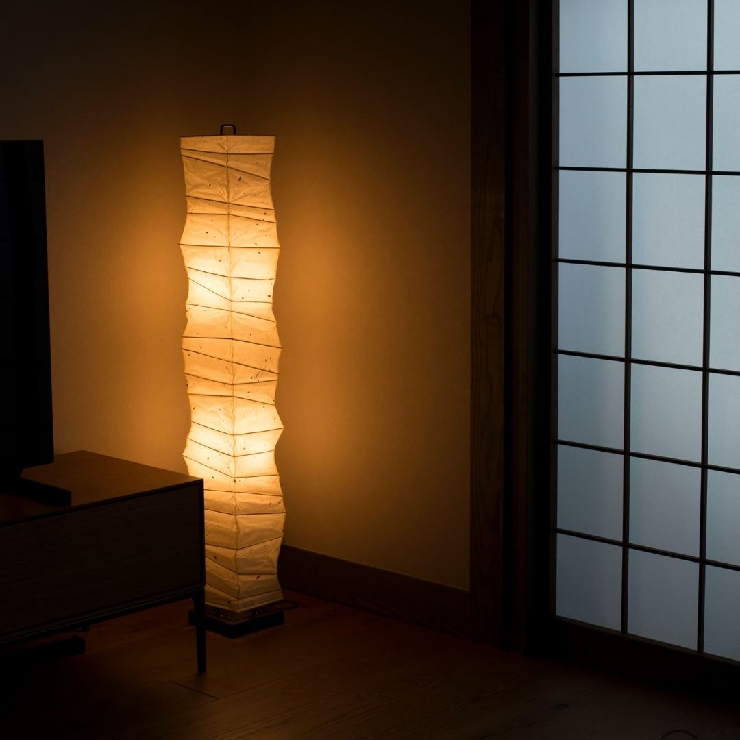"Lampadaire japonais « SLENDER » diffusant une lumière chaude dans le coin d'un salon de style japonais faiblement éclairé"