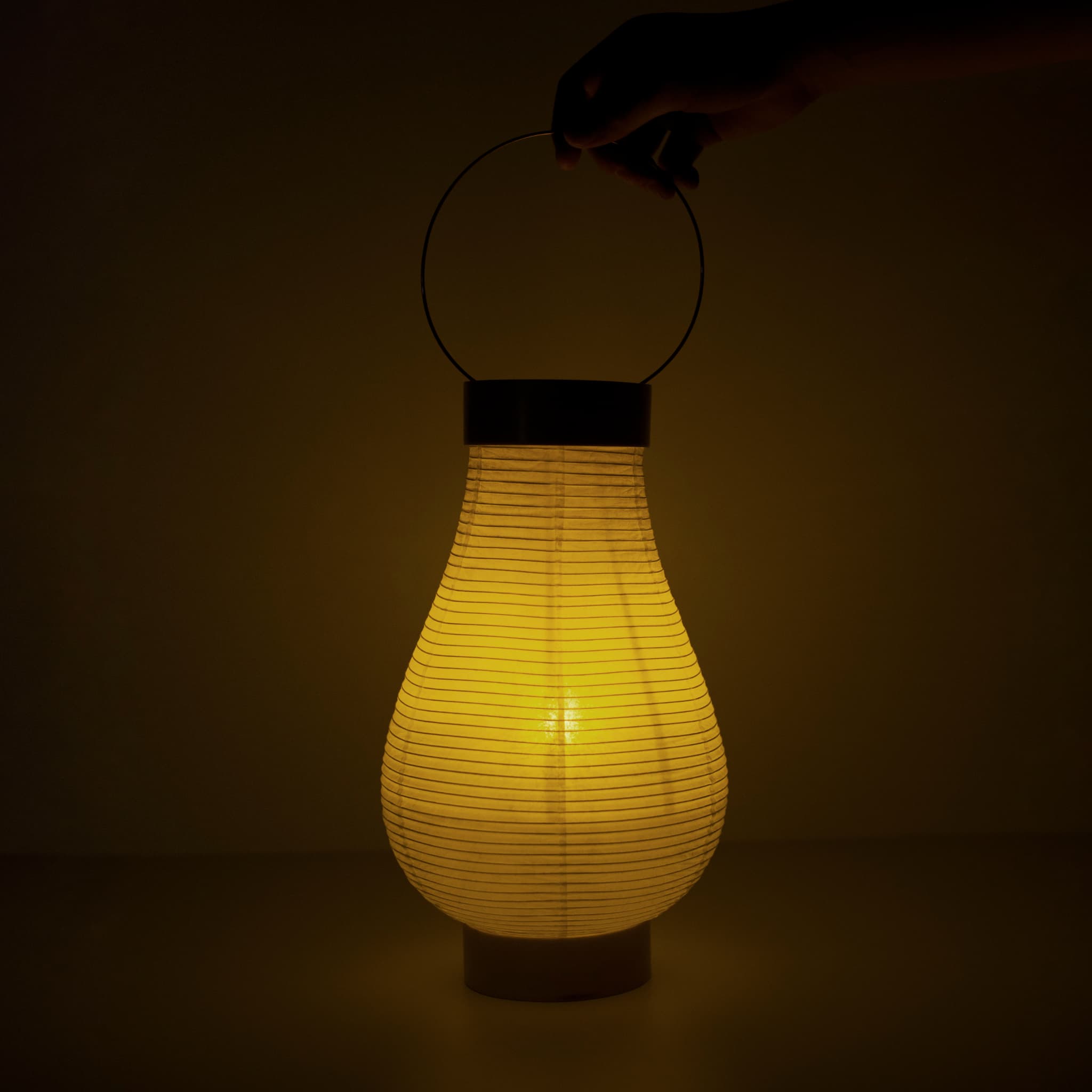 "Een traditionele Japanse papieren lantaarn met warme verlichting en een hand zichtbaar in een donkere kamer"