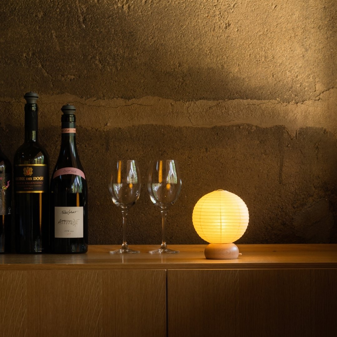 Japansk papir bordlampe "Mini Cirkel" med vinflasker og vinglas på en træhylde i et hjørne i et rum