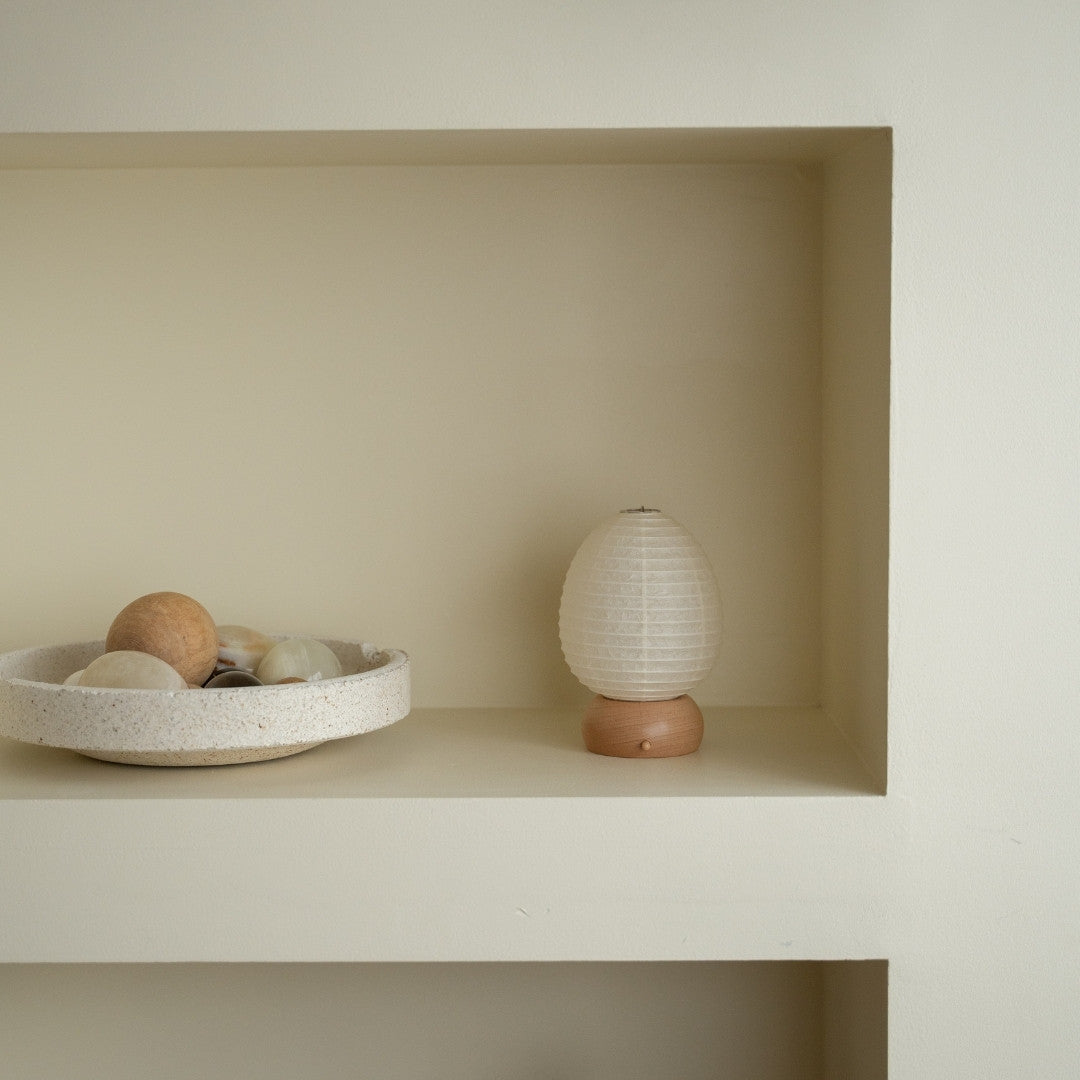 "Japanische Papier-Tischlampe „Mini Egg“ auf einem weißen Regal in einem Wohnzimmer im Japandi-Stil – Stilvolle Papierlampe für den Beistelltisch"