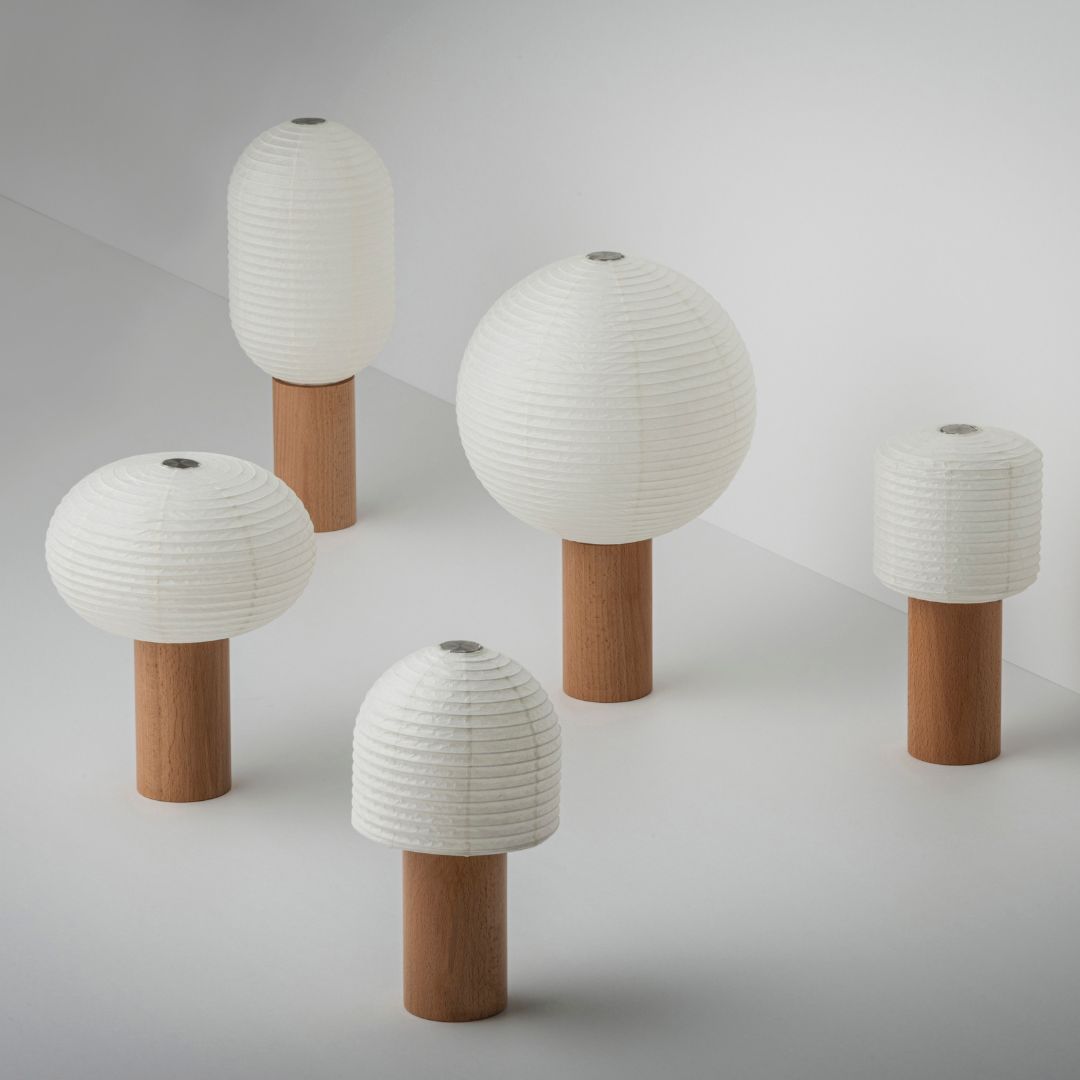 "Fünf Papier-Tischlampen, „TORCHIN“, mit schönem weißem Washi-Papier und braunen Holzgriffen, zufällig in einem hellweißen Raum angeordnet. Die Lampenschirme bestehen aus japanischem Washi-Papier von Yame-Chōchin-Laternen, und jede Lampe hat einen zylindrischen Holzgriff."