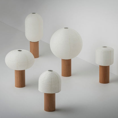 "Fünf Papier-Tischlampen, „TORCHIN“, mit schönem weißem Washi-Papier und braunen Holzgriffen, zufällig in einem hellweißen Raum angeordnet. Die Lampenschirme bestehen aus japanischem Washi-Papier von Yame-Chōchin-Laternen, und jede Lampe hat einen zylindrischen Holzgriff."
