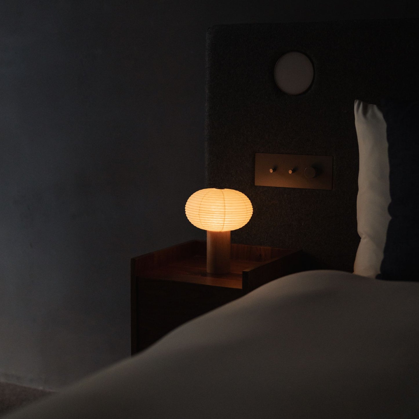 "Eine japanische Papier-Tischlampe „TORCHIN OVAL“ auf einem Nachttisch." 