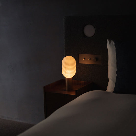 A Japanese paper touch lamp "TORCHIN VERTICAL" on a bedside table. 