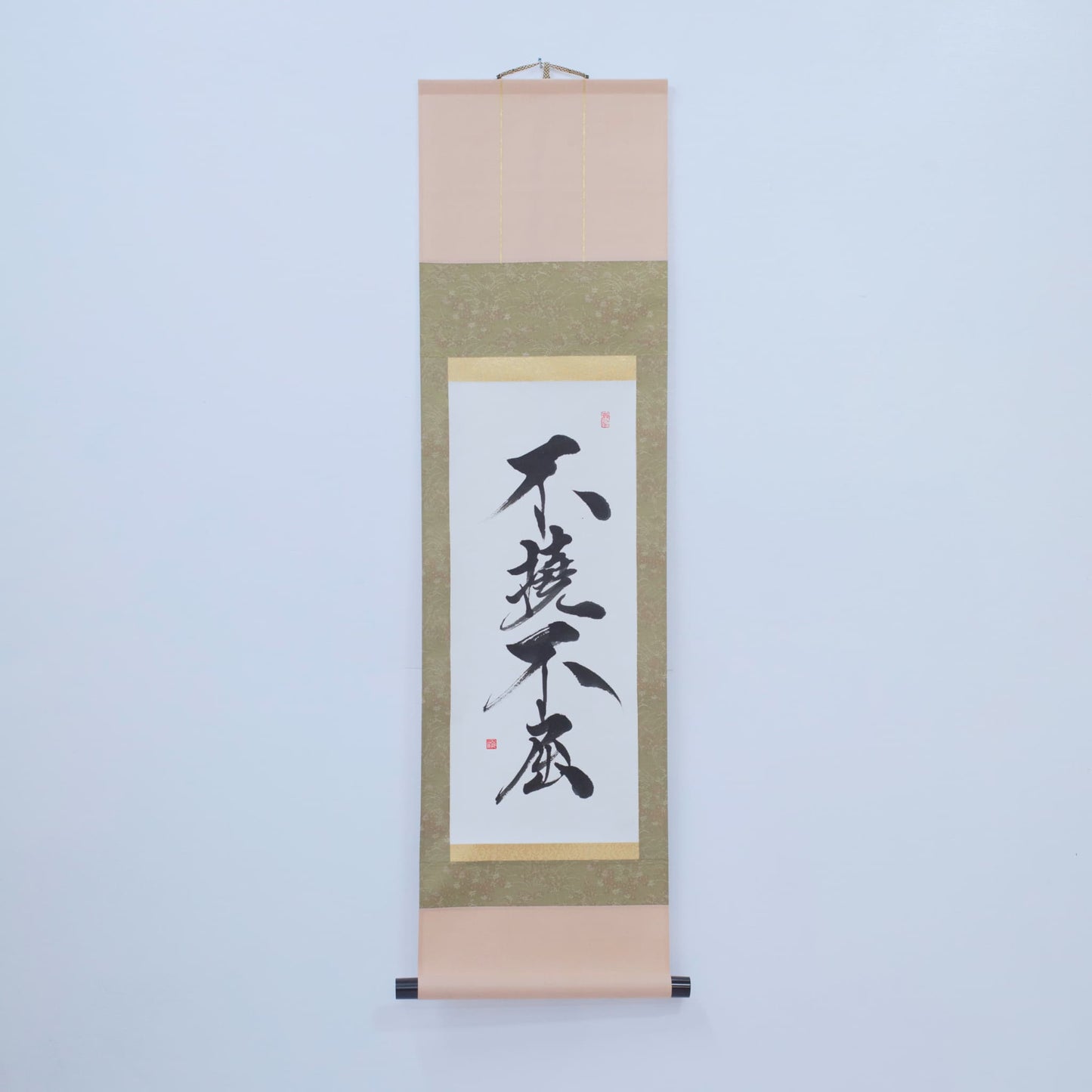 Eine braune, traditionelle japanische Hänge-Schriftrolle mit Kalligrafie von '不撓不屈' (Unbeugsamer Geist) auf Reispapier, ausgestellt an einer weißen Wand