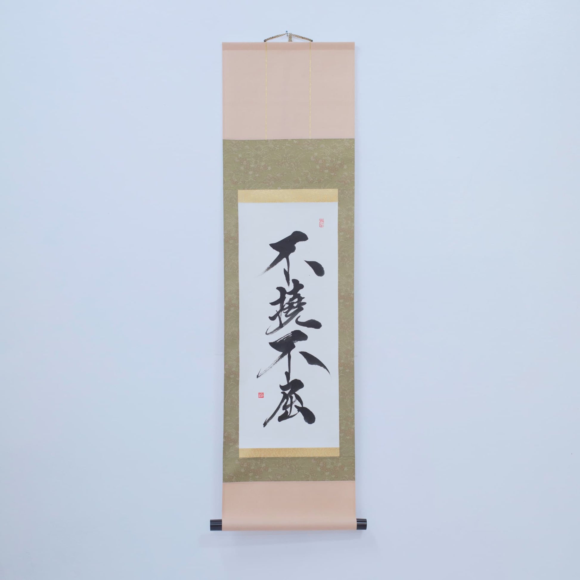 Eine braune, traditionelle japanische Hänge-Schriftrolle mit Kalligrafie von '不撓不屈' (Unbeugsamer Geist) auf Reispapier, ausgestellt an einer weißen Wand