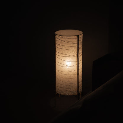 Salle faiblement éclairée avec un lampadaire japonais cylindrique en papier washi et un cadre en bambou, projetant une lueur chaleureuse dans une chambre japonaise