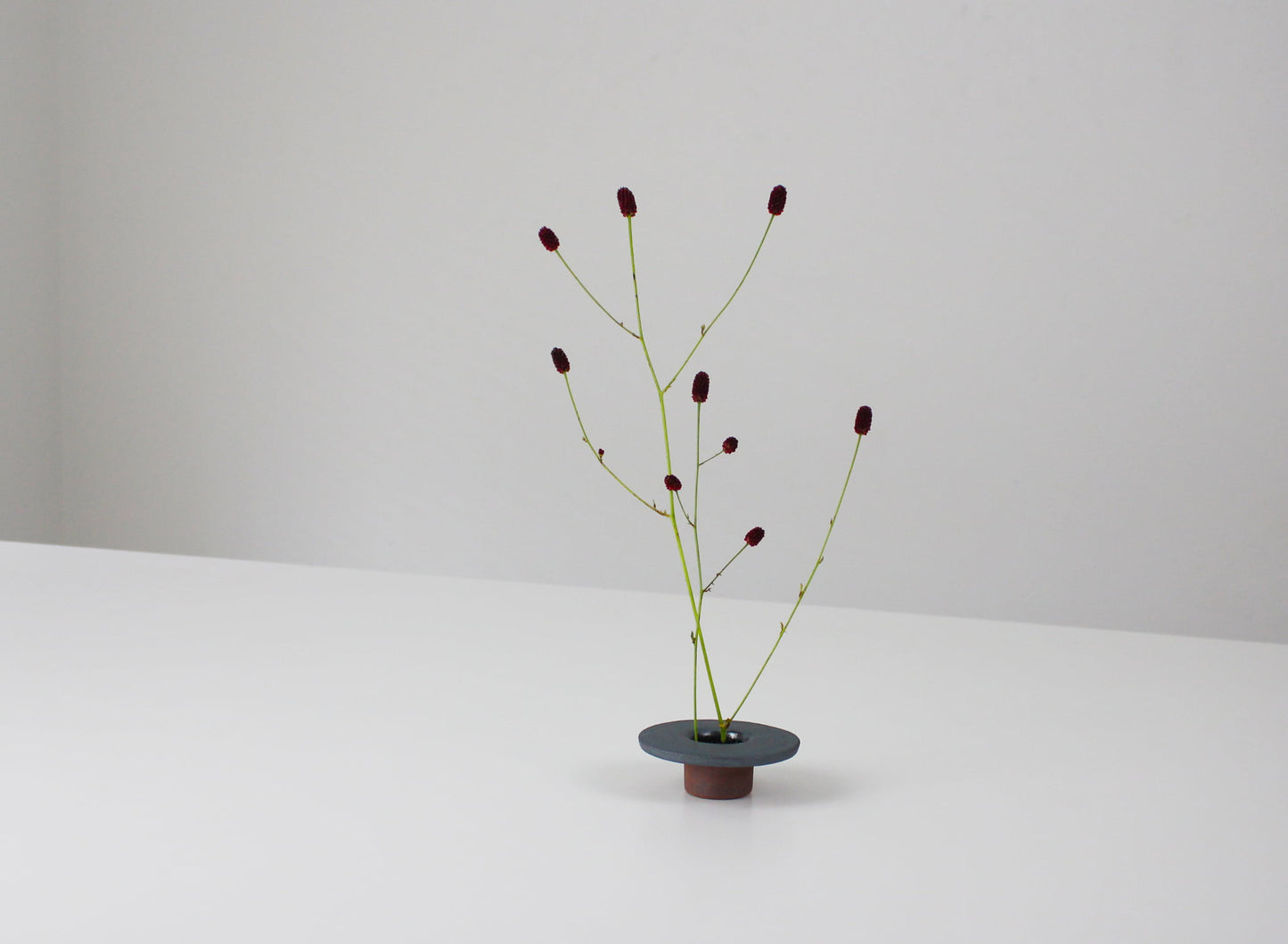 minimalistisk, sekskantet jernvase inspireret af traditionelle japanske tagsten, med et enkelt blomsterarrangement.