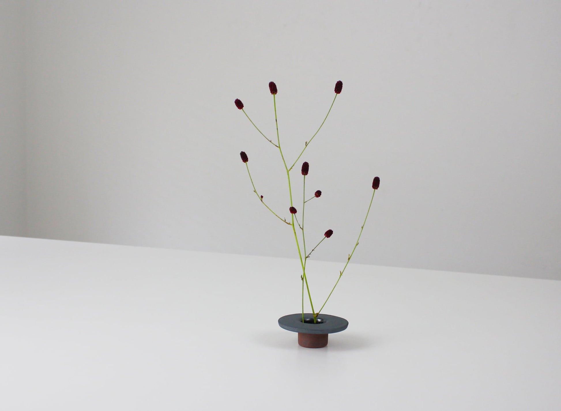 minimalistisk, sekskantet jernvase inspireret af traditionelle japanske tagsten, med et enkelt blomsterarrangement.