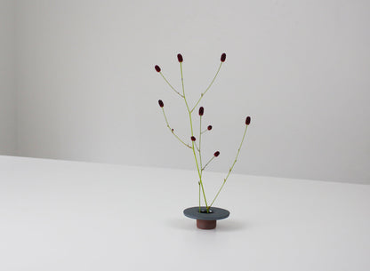 minimalistisk, sekskantet jernvase inspireret af traditionelle japanske tagsten, med et enkelt blomsterarrangement.