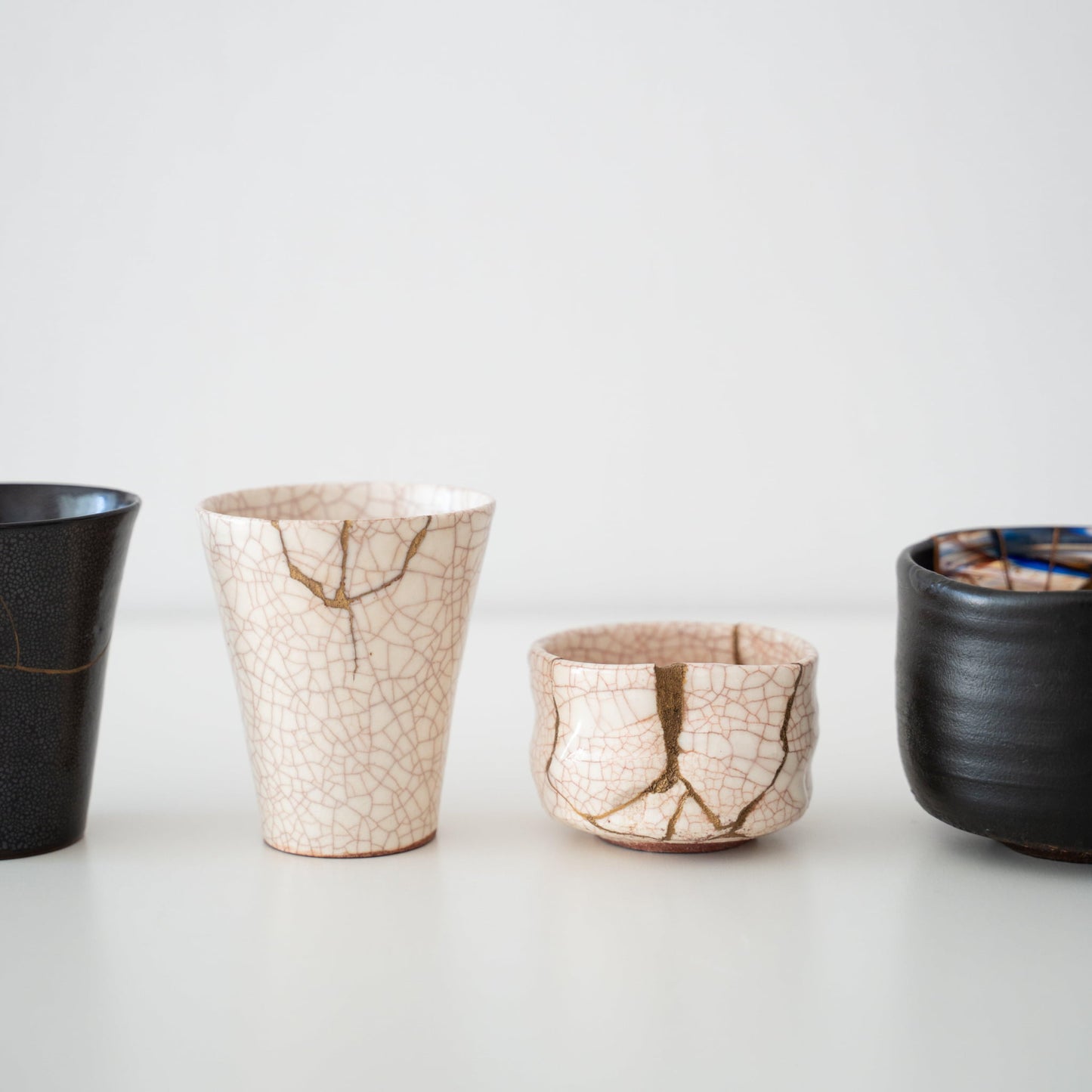Hvide og sorte kintsugi-kopper og te-skåle på et hvidt bord