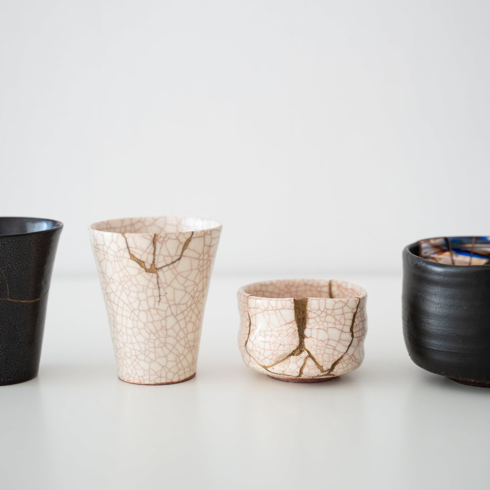 Hvide og sorte kintsugi-kopper og te-skåle på et hvidt bord