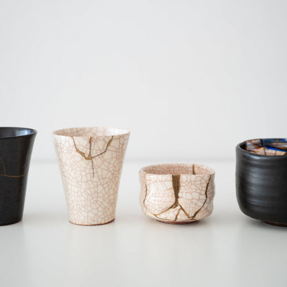 Hvide og sorte kintsugi-kopper og te-skåle på et hvidt bord