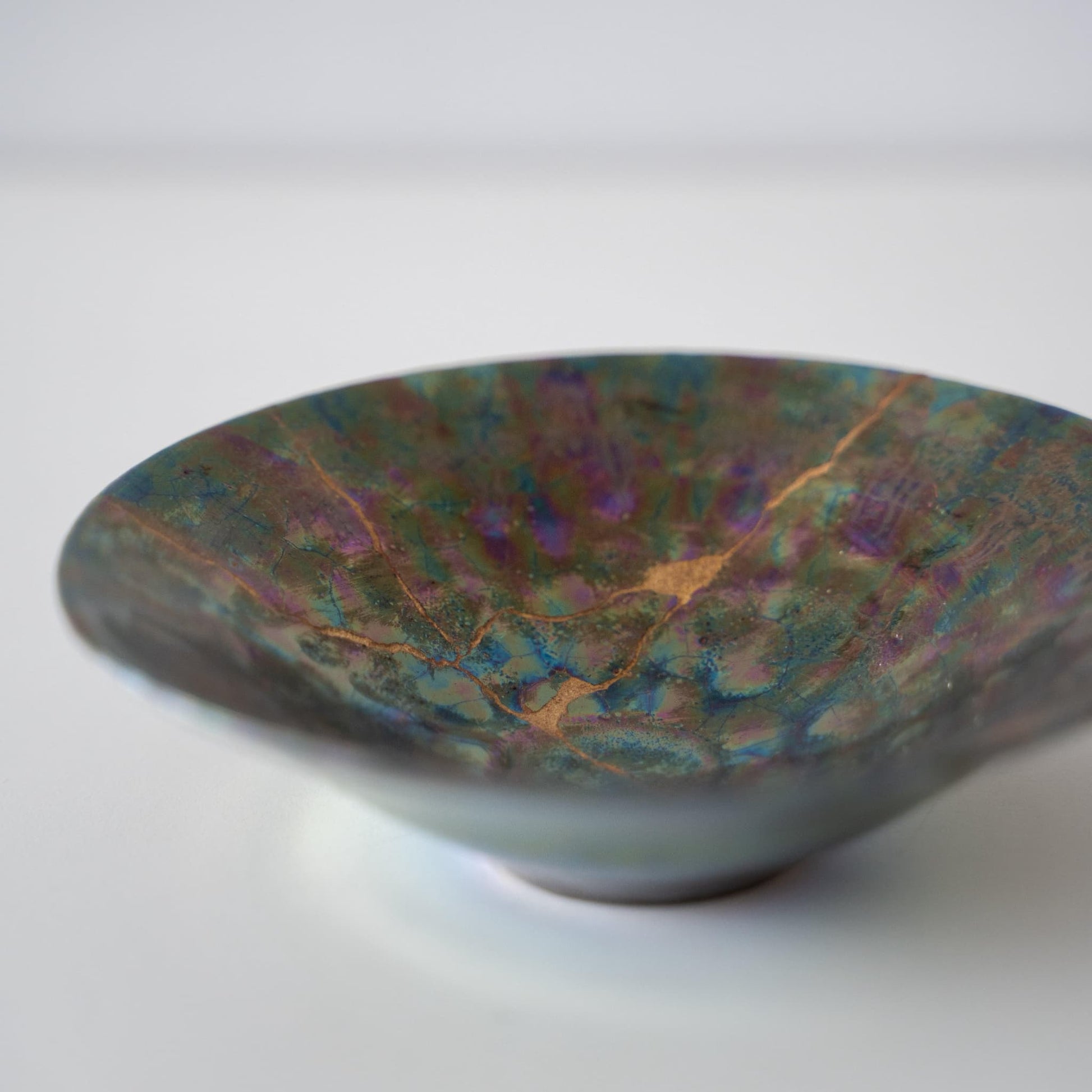 Gros plan du bol Kintsugi "Nébuleuse Verte" sur le côté, mettant en valeur les réparations Kintsugi complexes