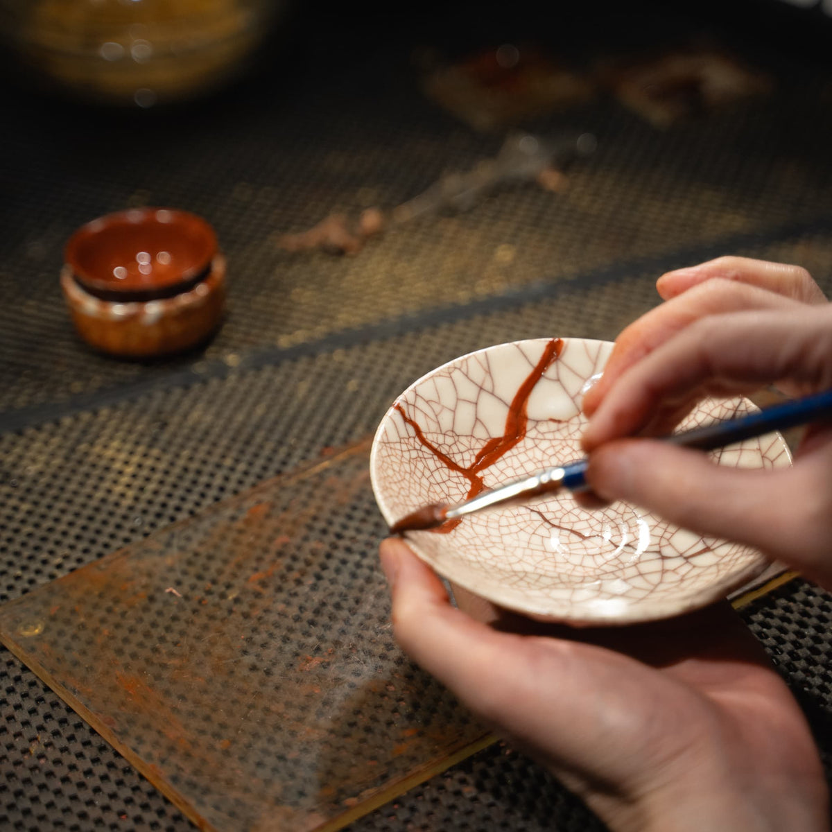 "De handen van een ambachtsman brengen Urushi-lak aan om een gebroken witte Kintsugi-kom te lijmen."