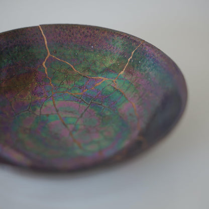 Iridescent skål repareret med kintsugi, den traditionelle japanske kunst at reparere knust keramik med guldlak.