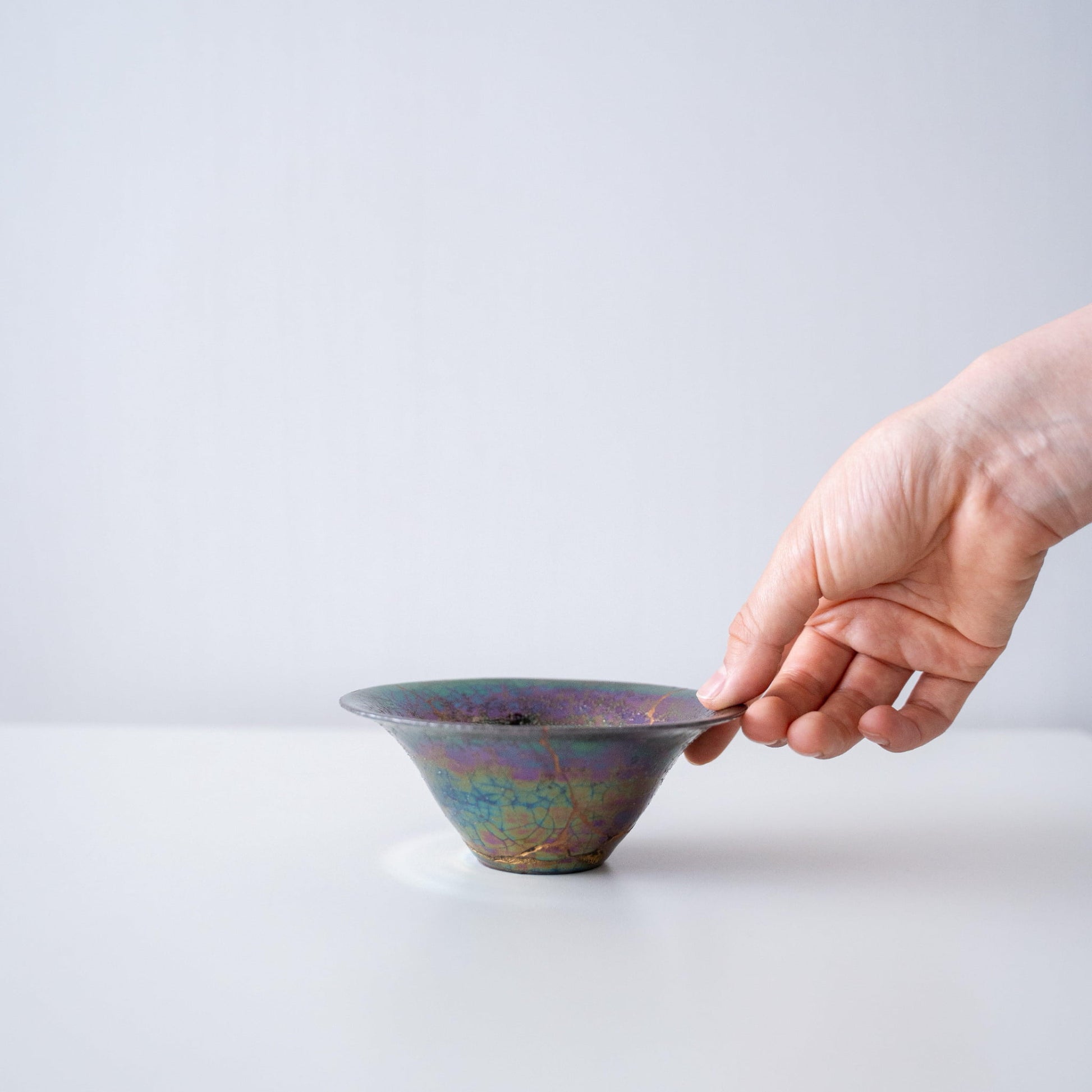 "Hand hält Kintsugi-Schale „Regenbogen-Schimmer“, zeigt ihre Größe und wie sie in die Hand passt"