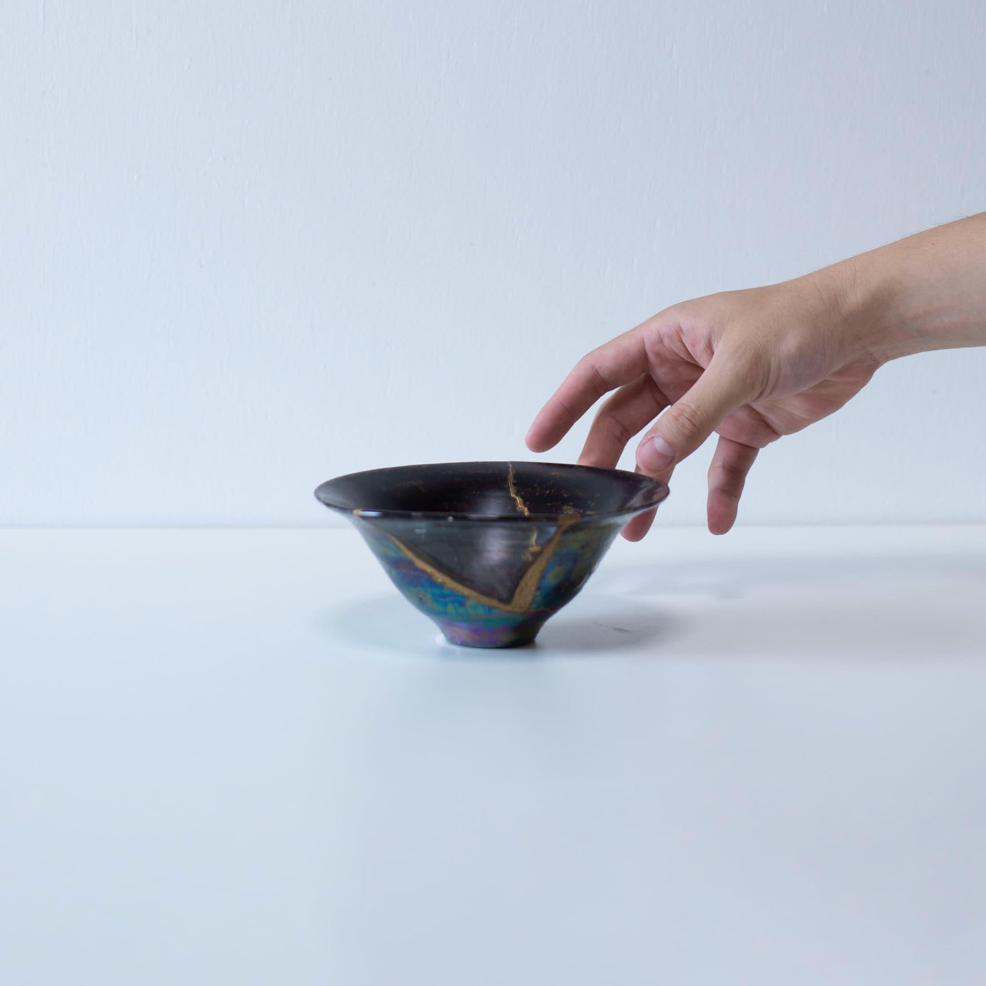 hånd, der forsigtigt holder en Kintsugi-skål, som viser den sarte natur af denne unikke reparationsteknik.