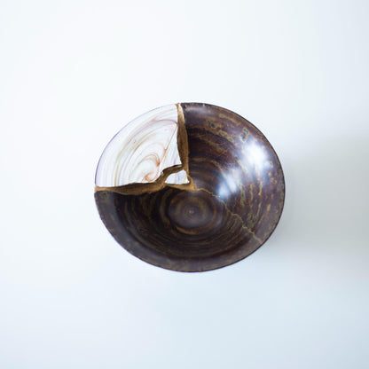 Eine Kintsugi-reparierte Schale mit einer schönen blauen Glasfüllung, die sich von einer warmbraunen Glasur abhebt und an die Rinde eines Kirschbaums erinnert.