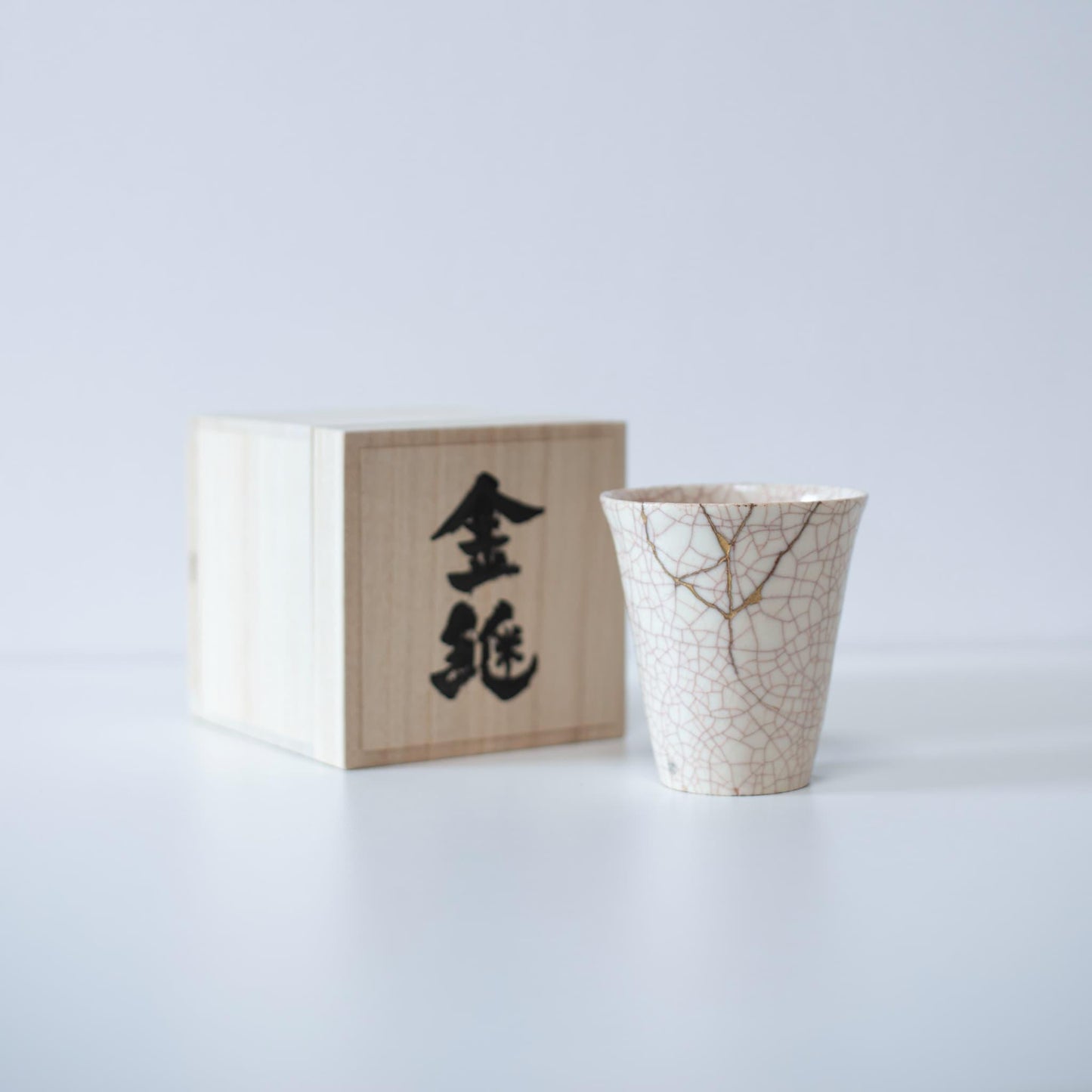 Hvid kop repareret med Kintsugi, en traditionel japansk teknik, præsenteret i en paulownia-trækasse med inskriptionen "Kintsugi".