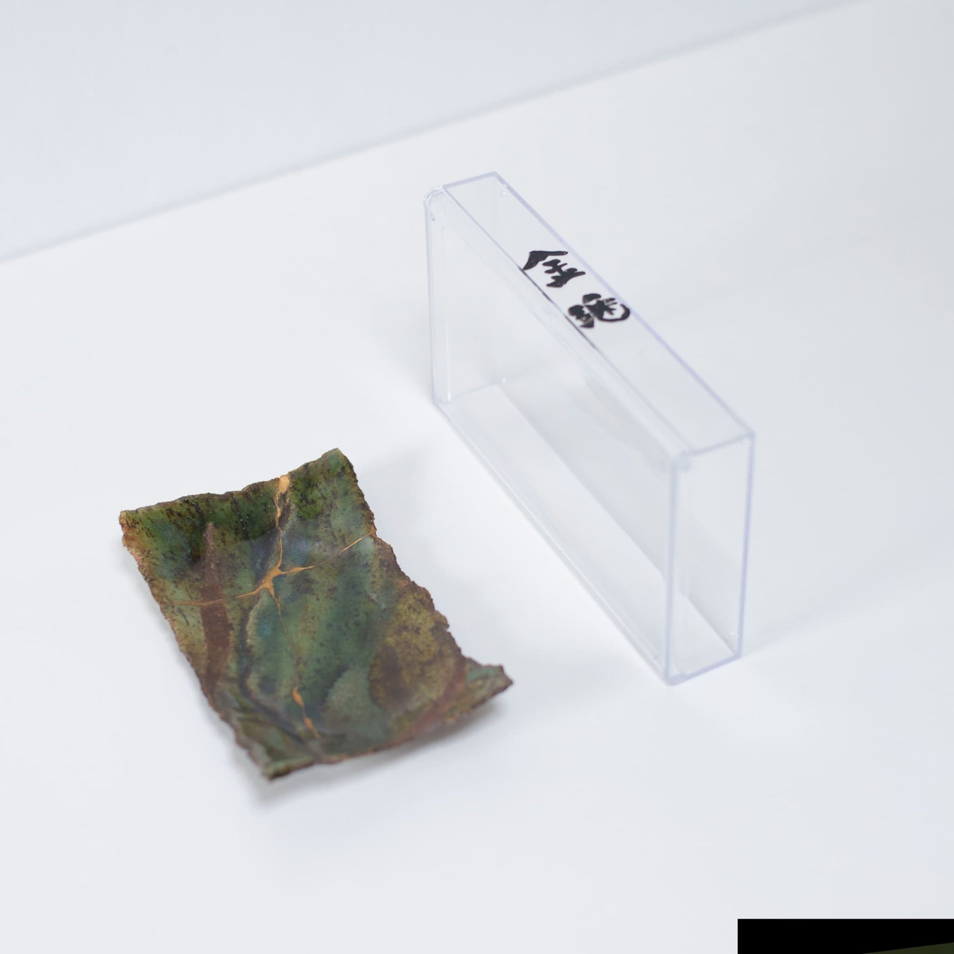 "Kintsugi-bord \"Oribe\" diepgroen 01 gepresenteerd in een doorzichtige koffer, bovenaanzicht."