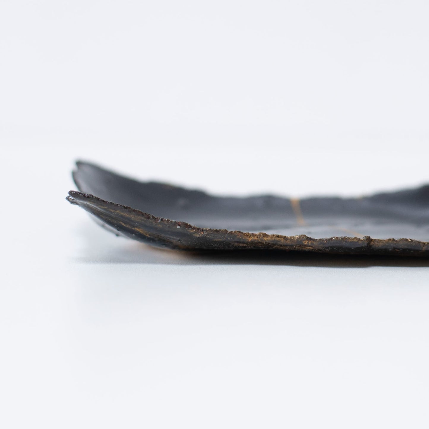 "Close-up van het zijaanzicht van Kintsugi-bord 'Tenmoku' Zwart 01, met nadruk op de textuur."