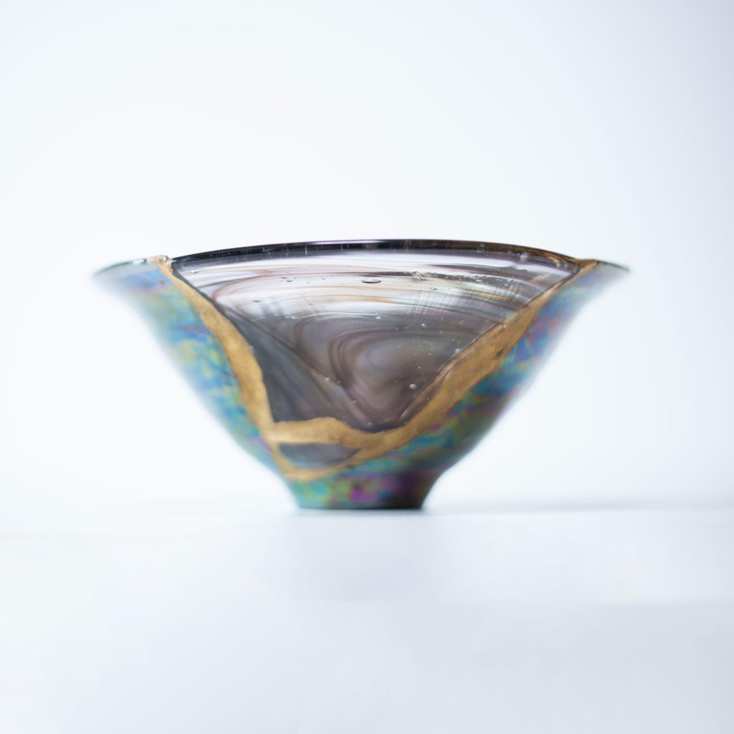 Nahaufnahme einer Kintsugi-reparierten Schale, die die komplizierten Details der Goldintarsien und den Kontrast zwischen brauner Keramik und blauem Glas zeigt.