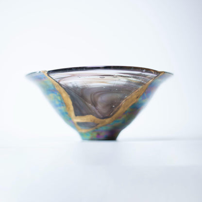Nahaufnahme einer Kintsugi-reparierten Schale, die die komplizierten Details der Goldintarsien und den Kontrast zwischen brauner Keramik und blauem Glas zeigt.