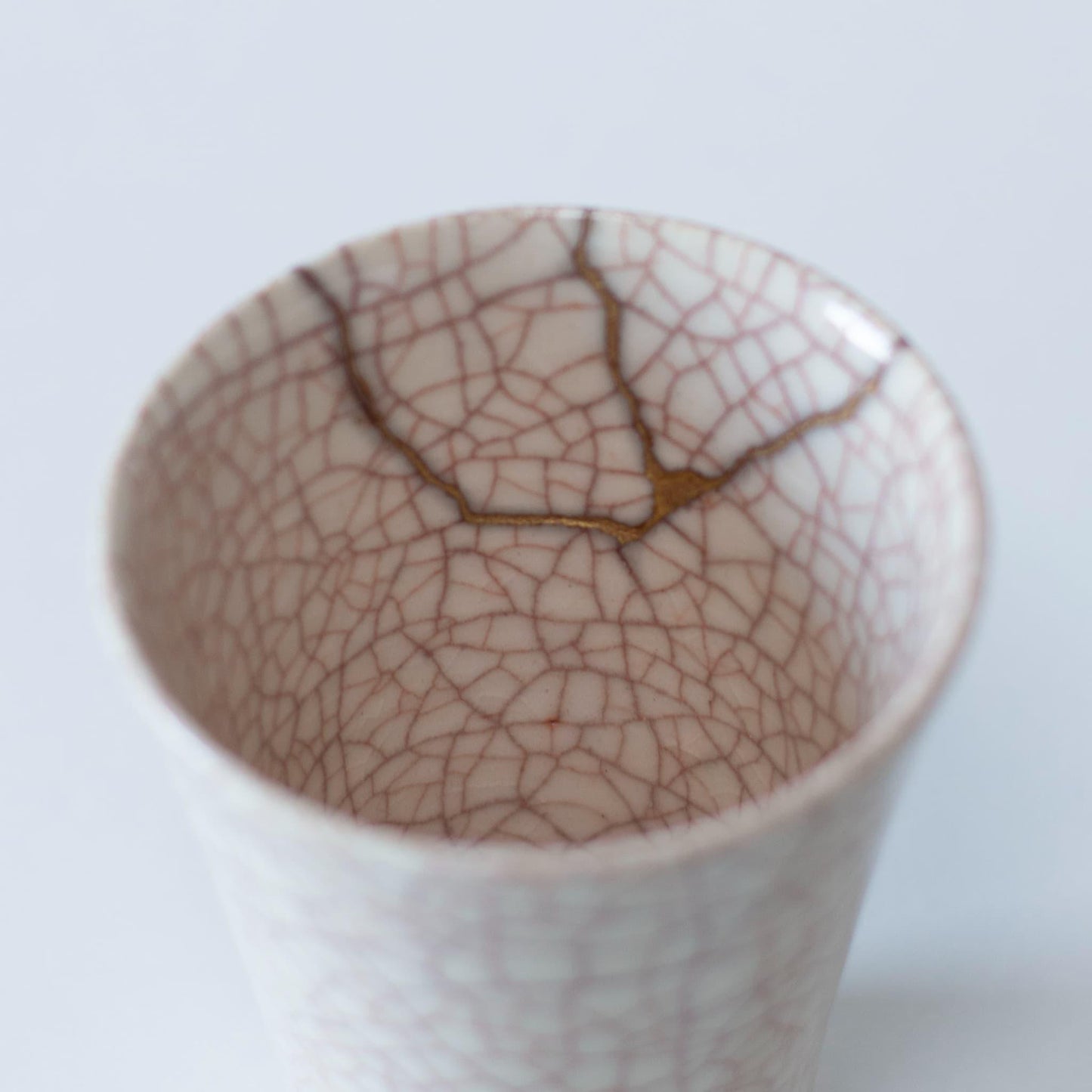 Et nærbillede af den delikate kintsugi-reparation på indersiden af en hvid keramik kop, der viser den japanske æstetik af wabi-sabi.