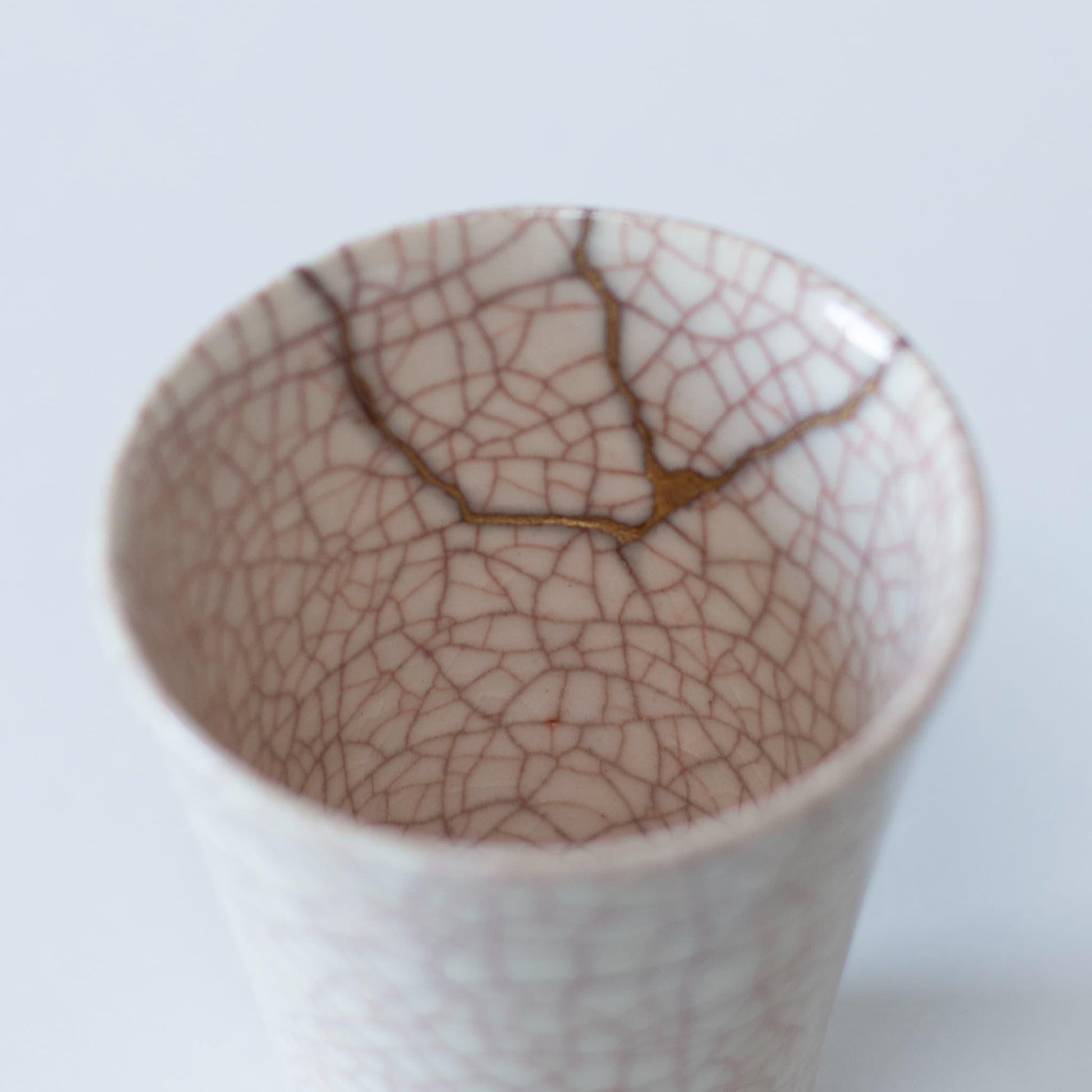 Et nærbillede af den delikate kintsugi-reparation på indersiden af en hvid keramik kop, der viser den japanske æstetik af wabi-sabi.