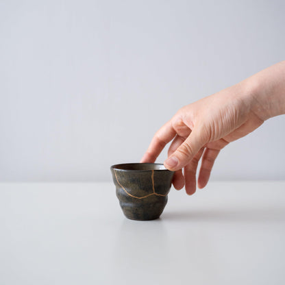 "Hand die Kintsugi Sake Cup \"Thunder Moss\" vasthoudt, met weergave van de grootte en hoe deze in de hand past"