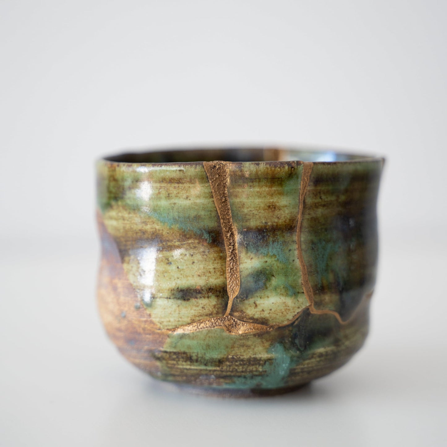 Tæt på siden af Kintsugi-tekop "Deep Forest Oribe", der fremhæver de indviklede Kintsugi-reparationer