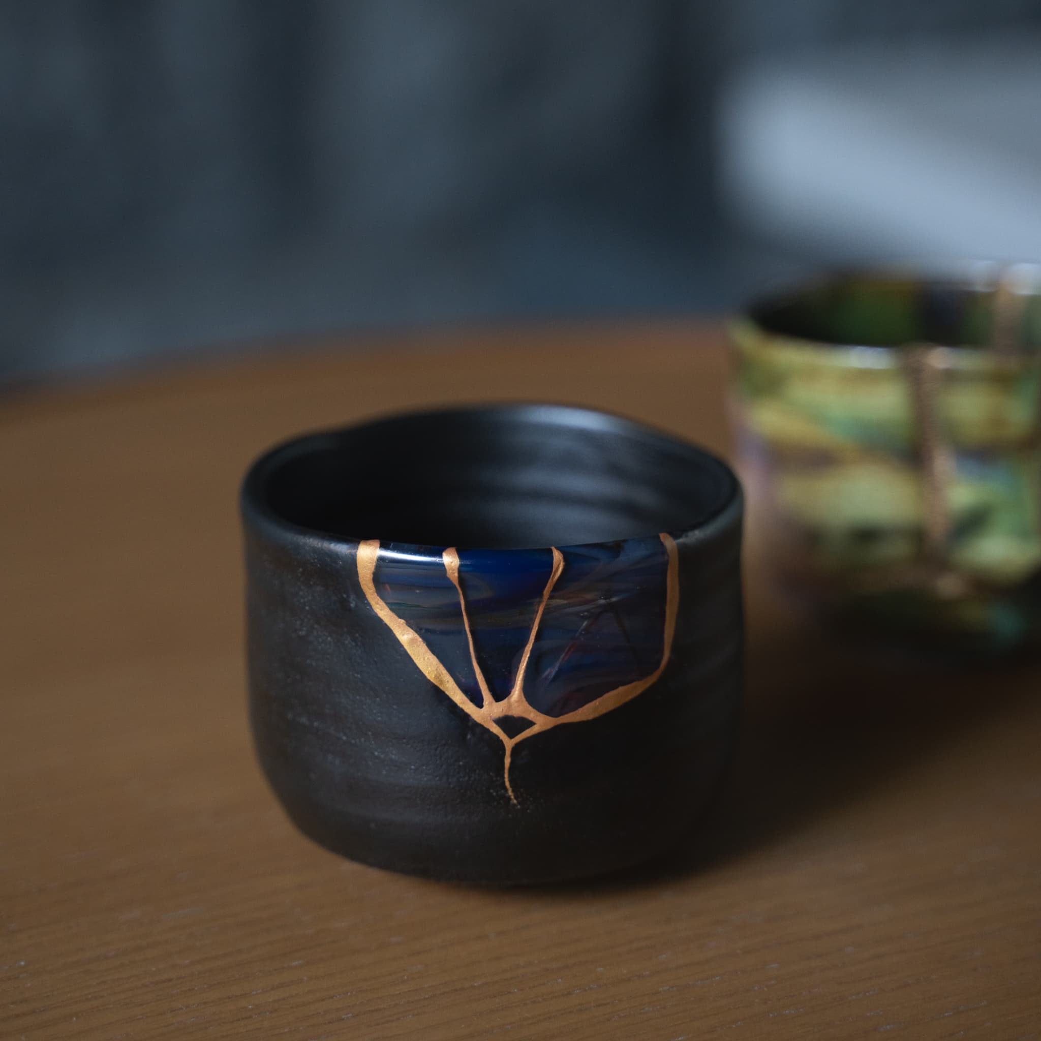 Beautiful black kintsugi tea bowl with gold repairs, displayed on a wooden table