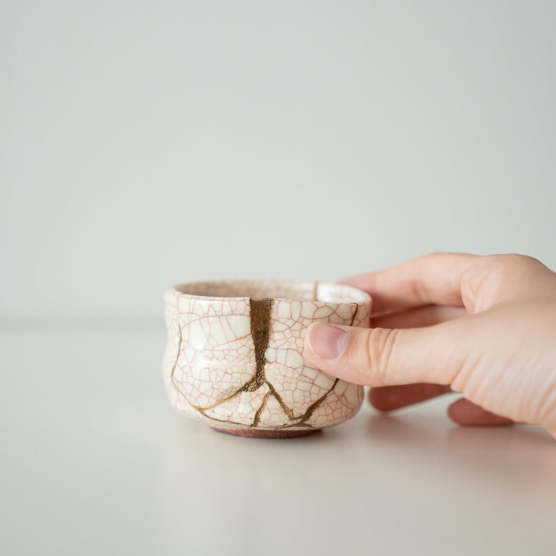 Hånd, der holder Kintsugi-tekop "Vermilion Crackle", der viser dens størrelse og hvordan den passer i hånden