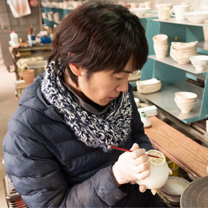 Buzan Kiln-håndværker maler i hånden en japansk Mino Ware matcha-skål i sit keramikstudie, der viser delikat penselstrøg og traditionelt håndværk.