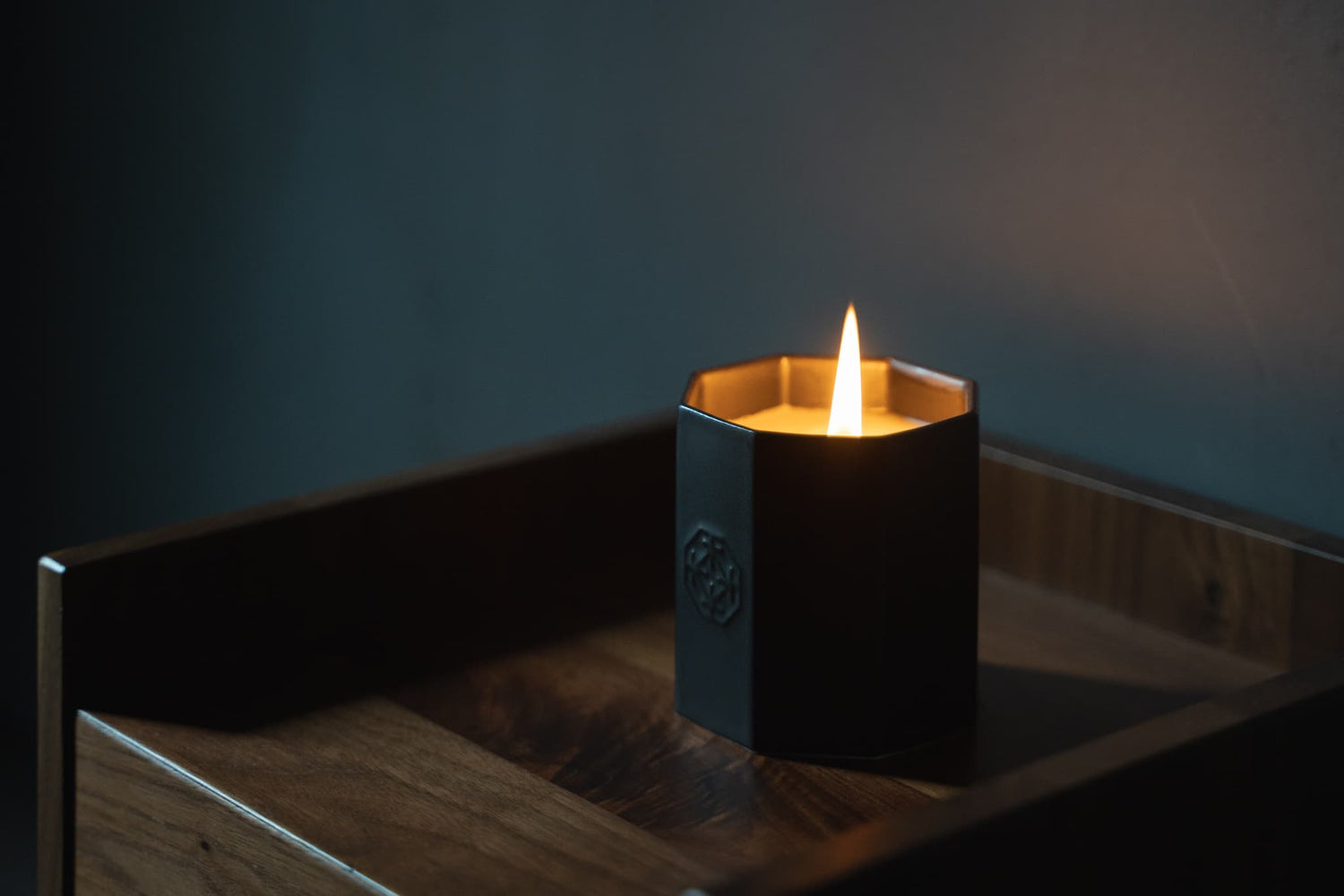 A lit black scented candle made of Arita ware, offering a relaxing wooden scent.