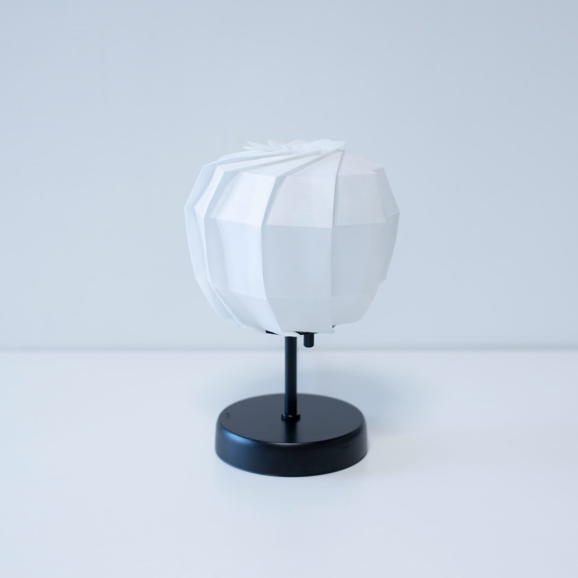 "Stijlvolle origami tafellamp met een zwarte standaard en een sferische witte lampenkap, vervaardigd uit ingewikkeld gevouwen washipapier."