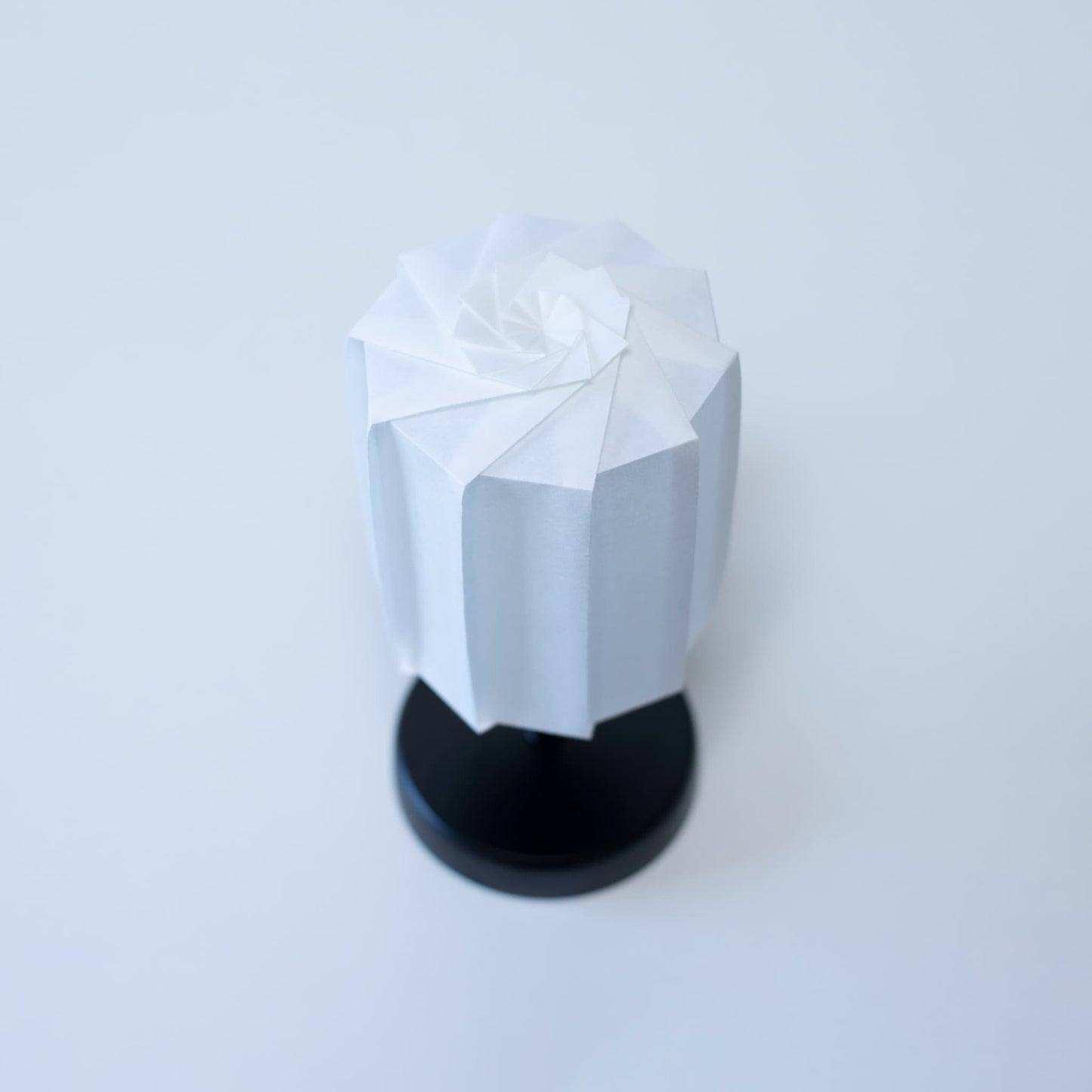 "Originele tafellamp \"tutu\" met een zwarte standaard en een witte cilindrische lampenkap van geplooid washipapier, voor een moderne toets in elke kamer."