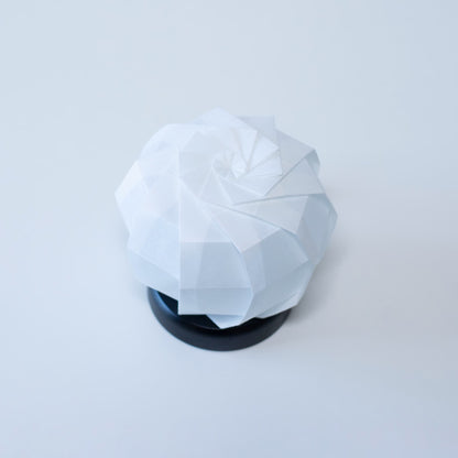 Stijlvolle Origami tafellamp met een zwarte voet en een witte sferische lampenkap van getextureerd washipapier.
