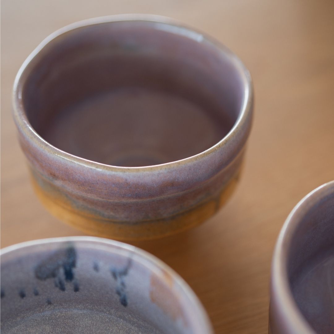 Nærbillede af en japansk matcha-skål i farven Pale Violet Haze fra Shinzan Kiln, der fremhæver den blanke lyse violette glasur, der blander sig med varme jordfarvede brune toner, hvilket indkapsler Wabi Sabi-æstetikken.