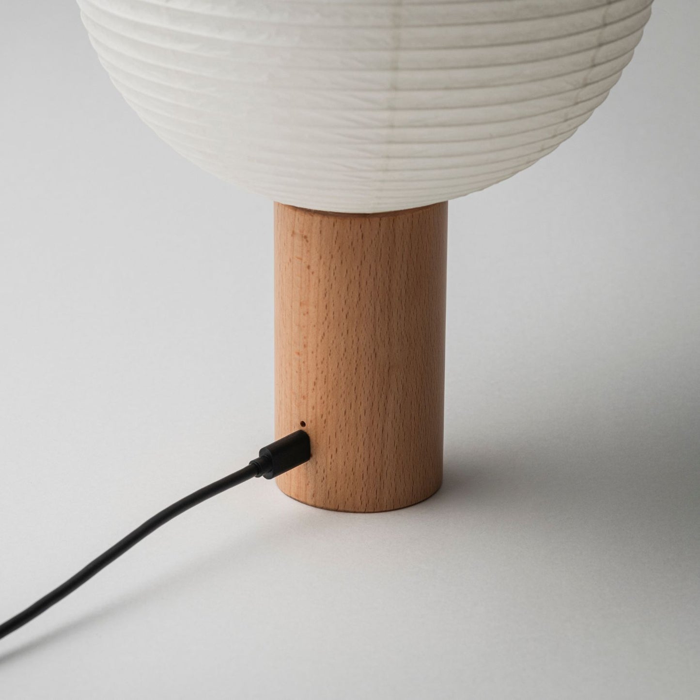 Eine tragbare Papierlampe mit Holzsockel und Ladeanschluss, verbunden mit einem Ladekabel