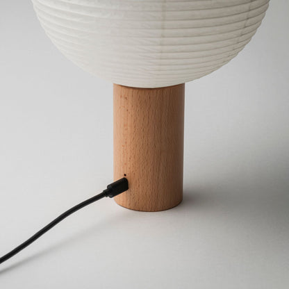 Eine tragbare Papierlampe mit Holzsockel und Ladeanschluss, verbunden mit einem Ladekabel