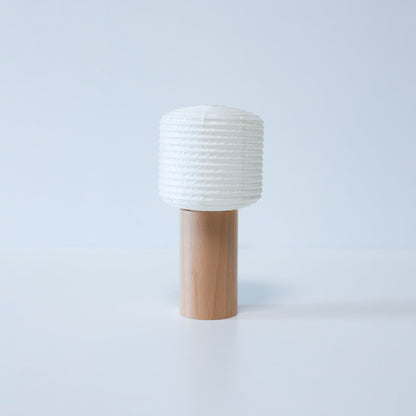 "Eine tragbare Papierlampe mit Holzsockel und zylindrischem Papieraufsatz vor weißem Hintergrund"